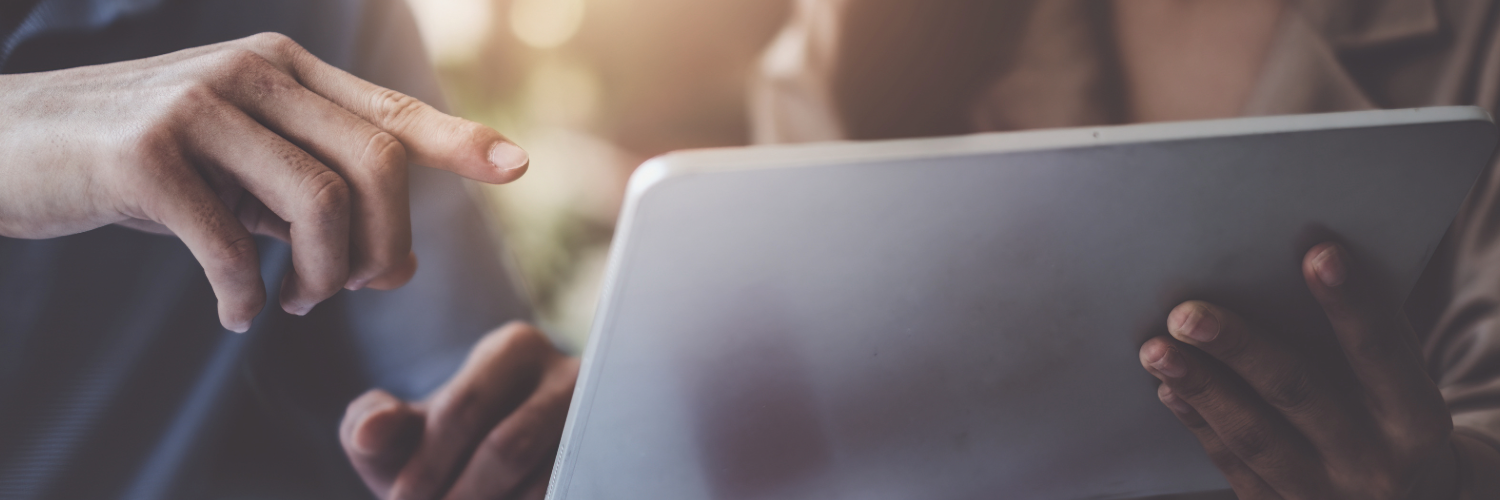 A hand holds a tablet, while another points towards the screen
