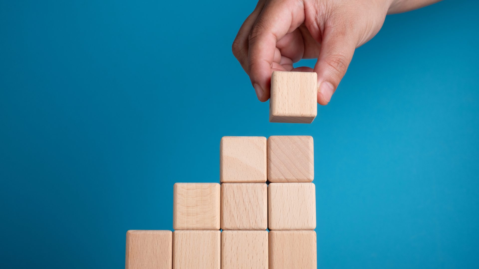 A hand placing a block atop a pile of wooden building blocks