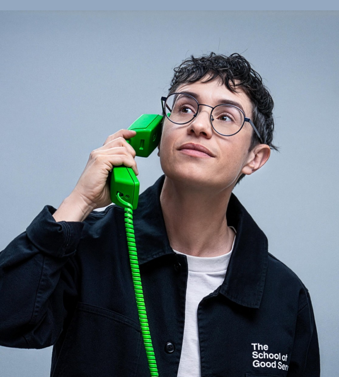 Studio portrait of Lou Downe holding a bright green telephone handset to one ear against a pale background.