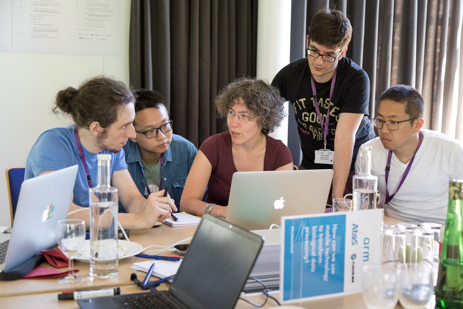 A group of people around a table, with laptops on the table. 