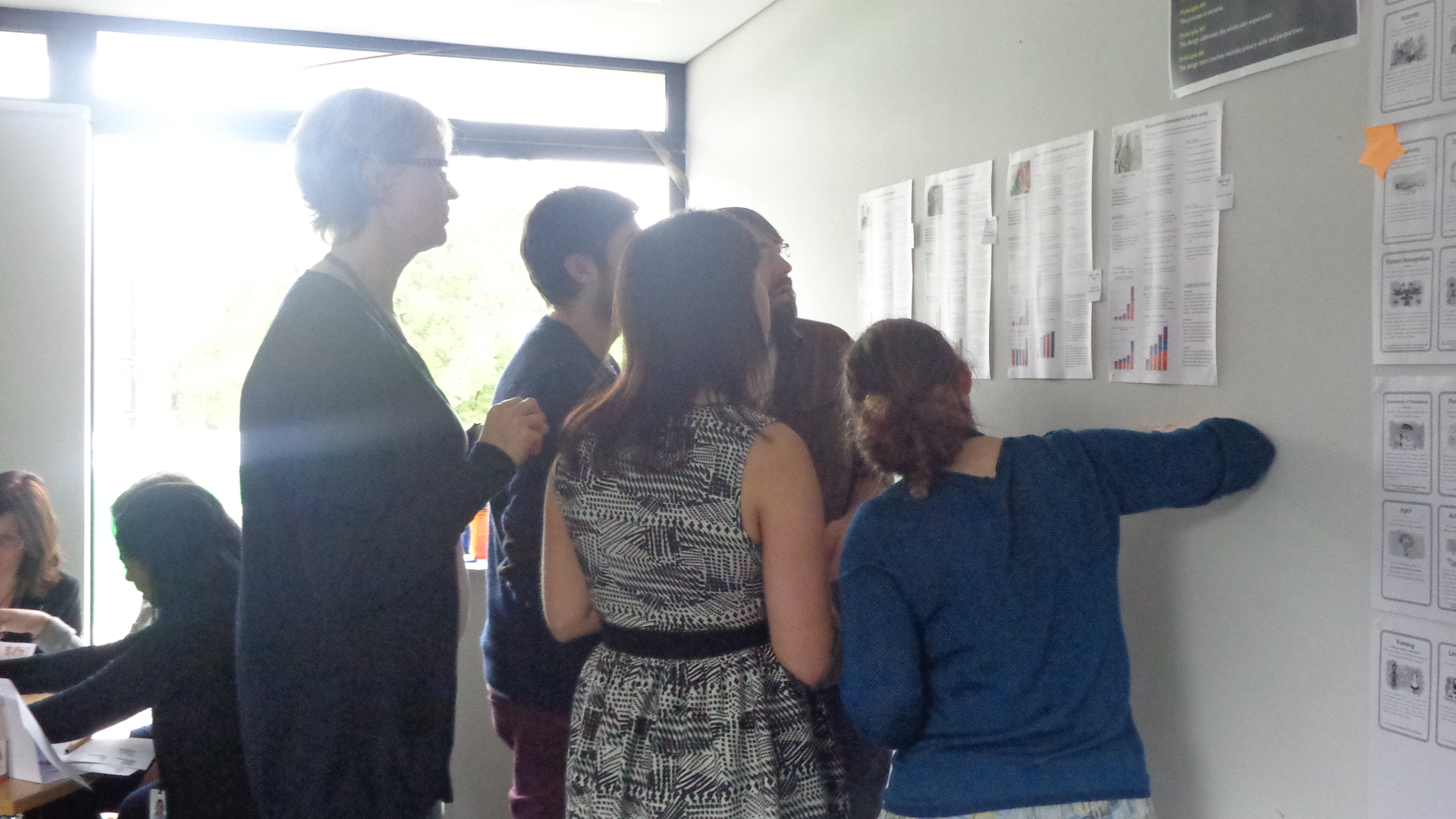 Five people looking at and discussing printed website pages on a wall in a design workshop