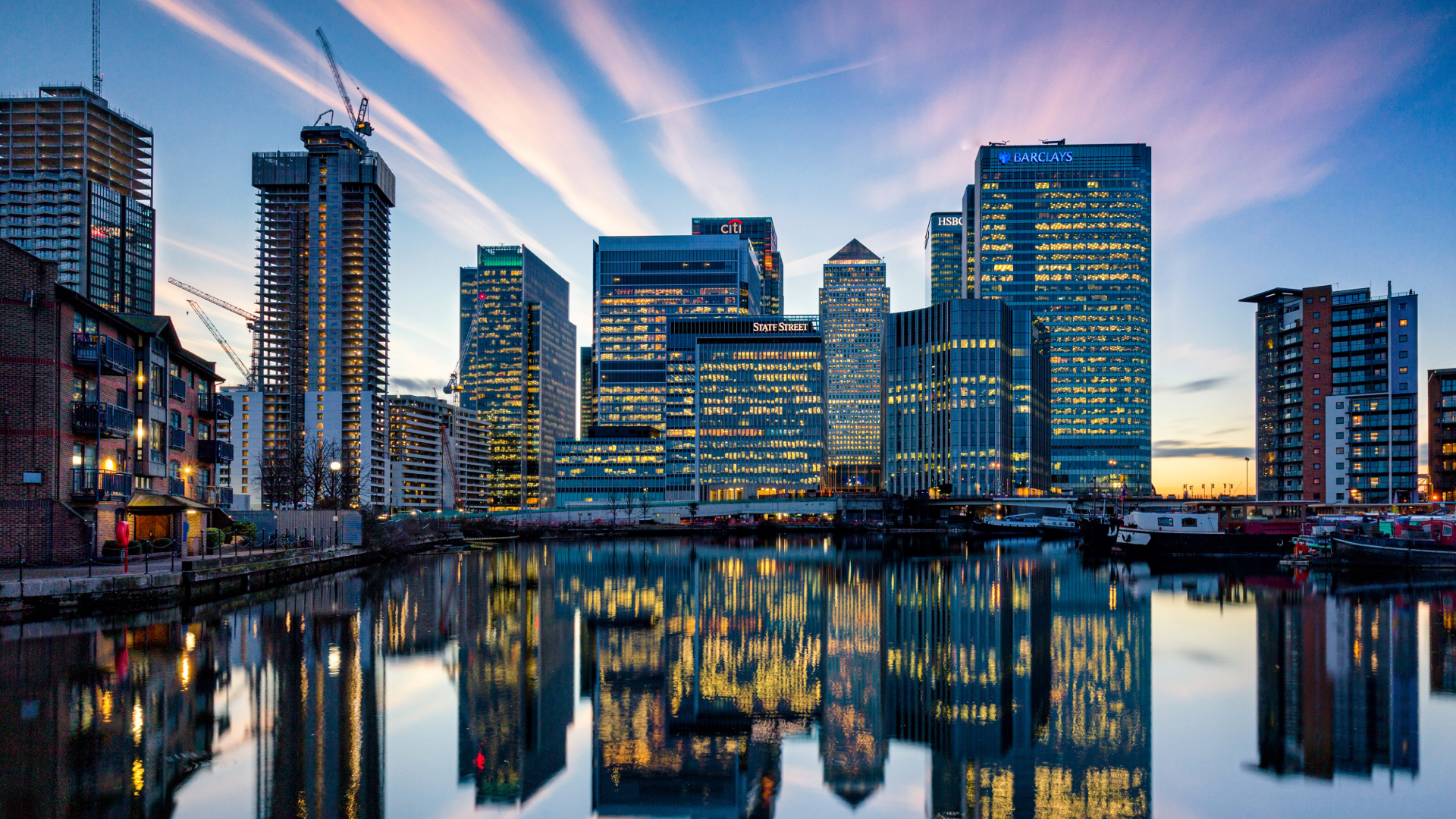 London's Canary Wharf skyline at dusk, with the buildings lit up against a purple sky. 