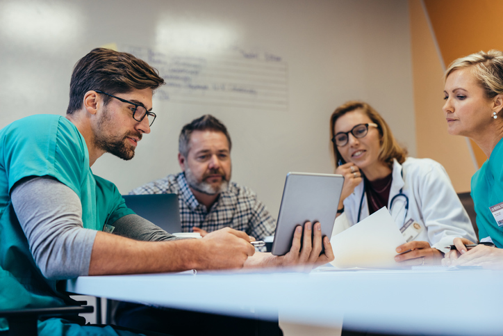 A group of doctors sat round a table looking at a tablet device
