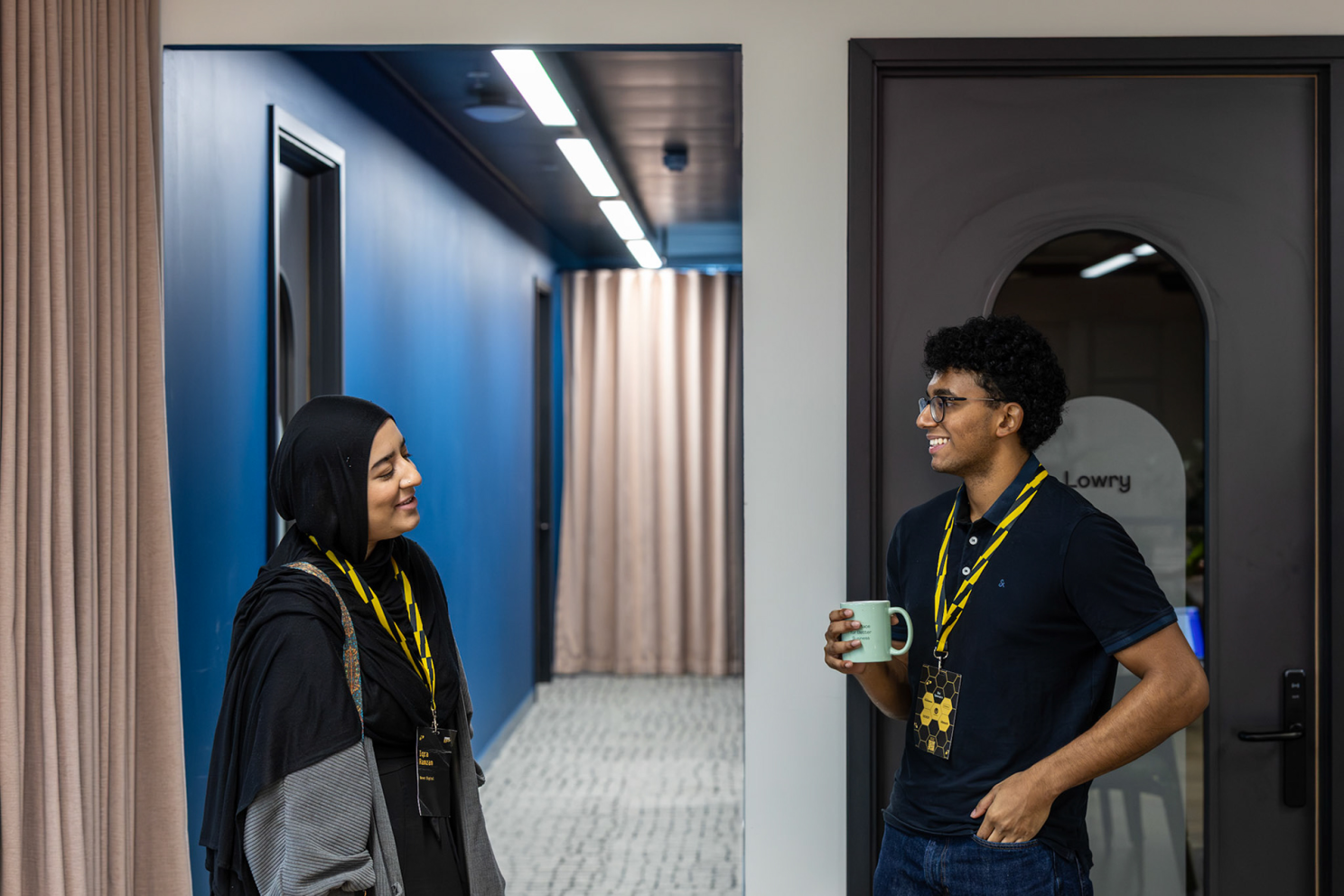 Nexer apprentices Iqra and Robin stand speaking. They are wearing Umbraco in the City, Manchester, conference lanyards