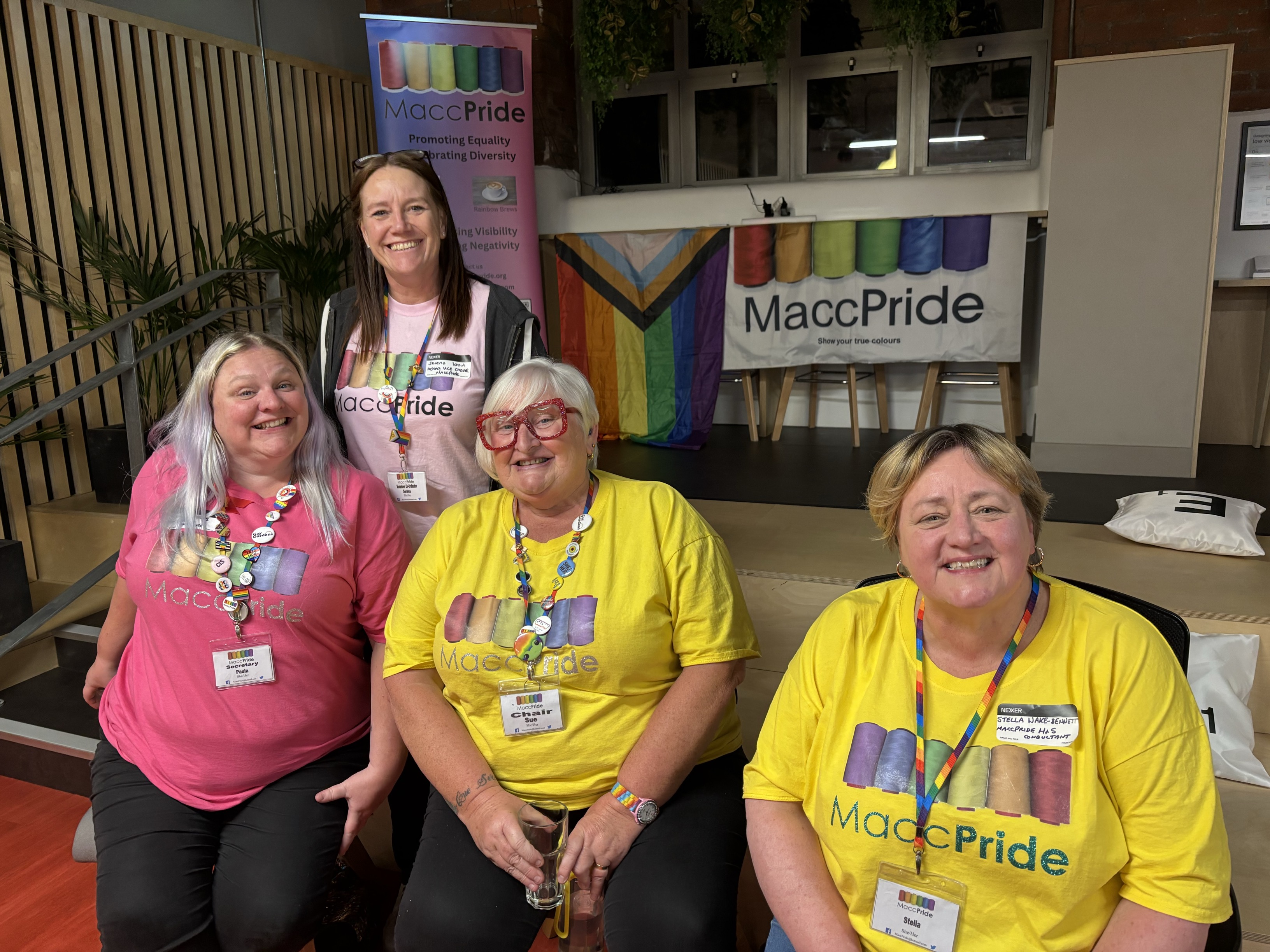 Four members of the Macc Pride team sit on the steps at the Nexer office. In the background are Macc Pride banners. 