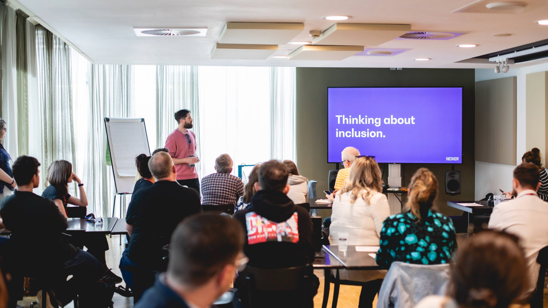 A workshop space at Camp Digital, with accessibility team lead Danny Lancaster addressing a room of seated people. Onscreen is a slide reading "Thinking about inclusion"